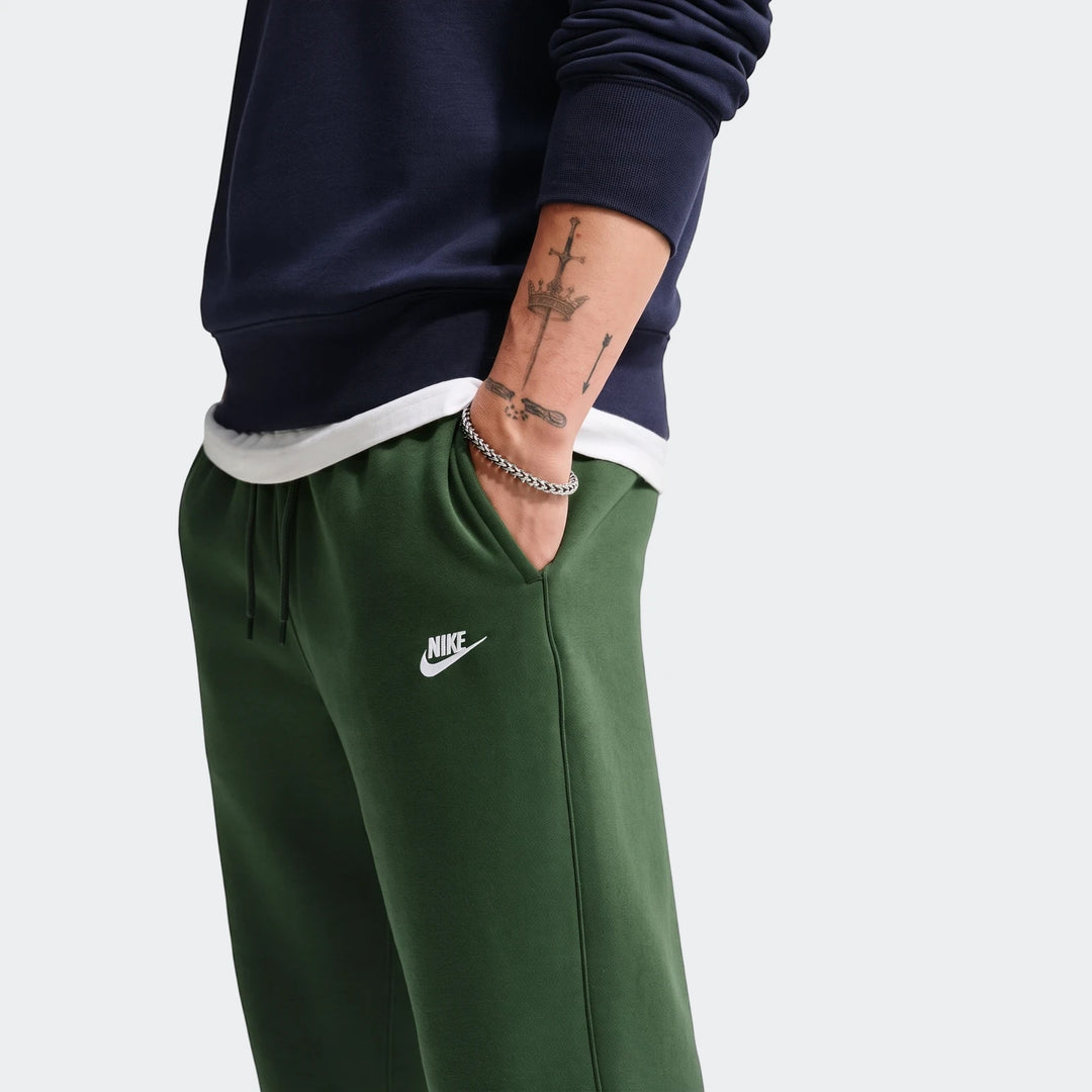 Close-up of a man wearing dark green Nike Sportswear Club Men's Joggers with a white logo and a navy sweatshirt.