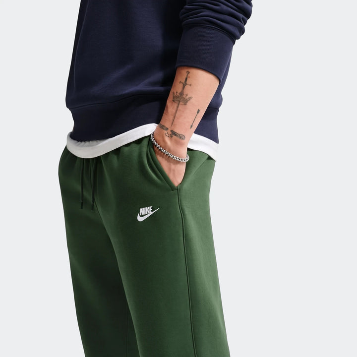 Close-up of a man wearing dark green Nike Sportswear Club Men's Joggers with a white logo and a navy sweatshirt.