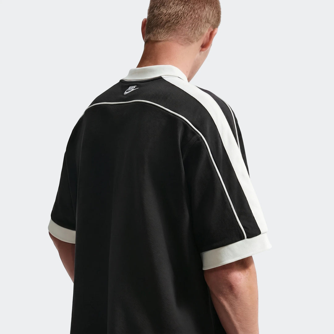 Men's Nike Sportswear Club oversized short-sleeve polo shirt in black with white collar and stripes, seen from the back.