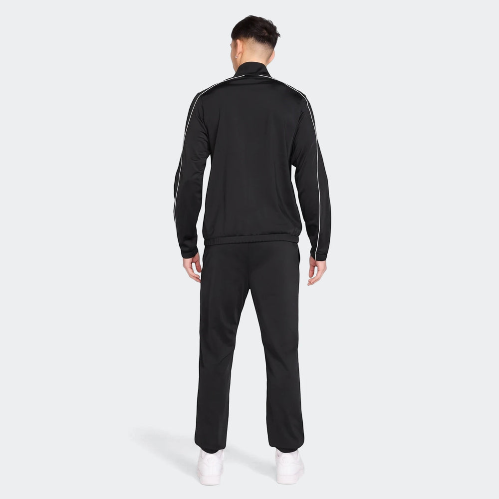Rear view of a male model wearing a black Nike Sportswear Club poly-knit tracksuit with white piping and white sneakers.