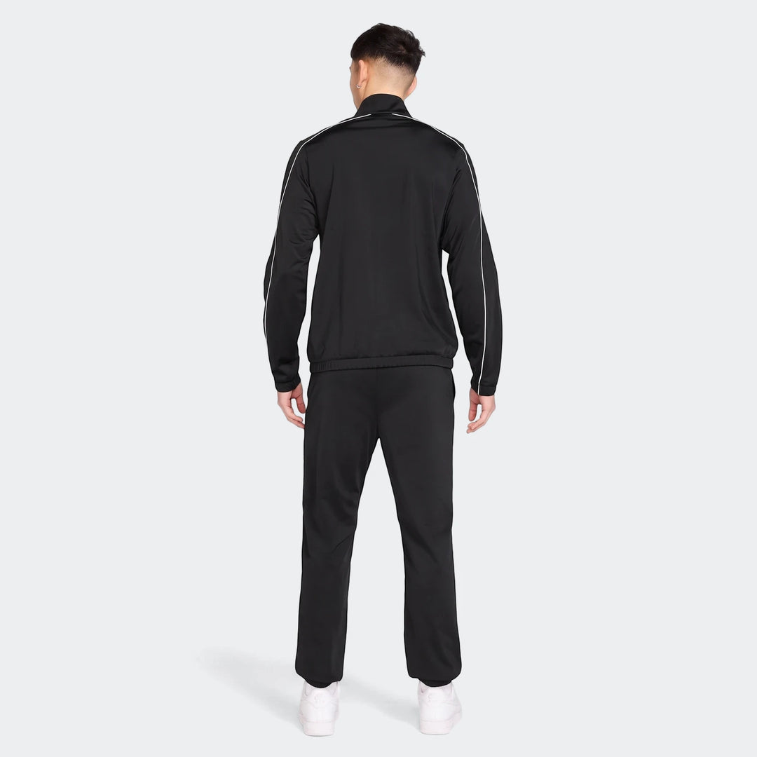 Rear view of a male model wearing a black Nike Sportswear Club poly-knit tracksuit with white piping and white sneakers.