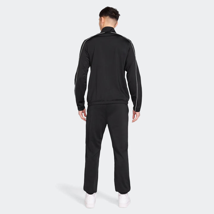 Rear view of a male model wearing a black Nike Sportswear Club poly-knit tracksuit with white piping and white sneakers.