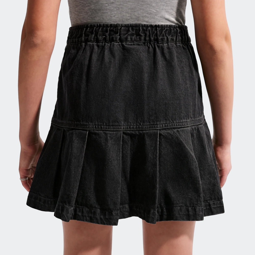 Back view of a Nike Sportswear Big Kids' (Girls') black denim pleated skirt, worn by a child.