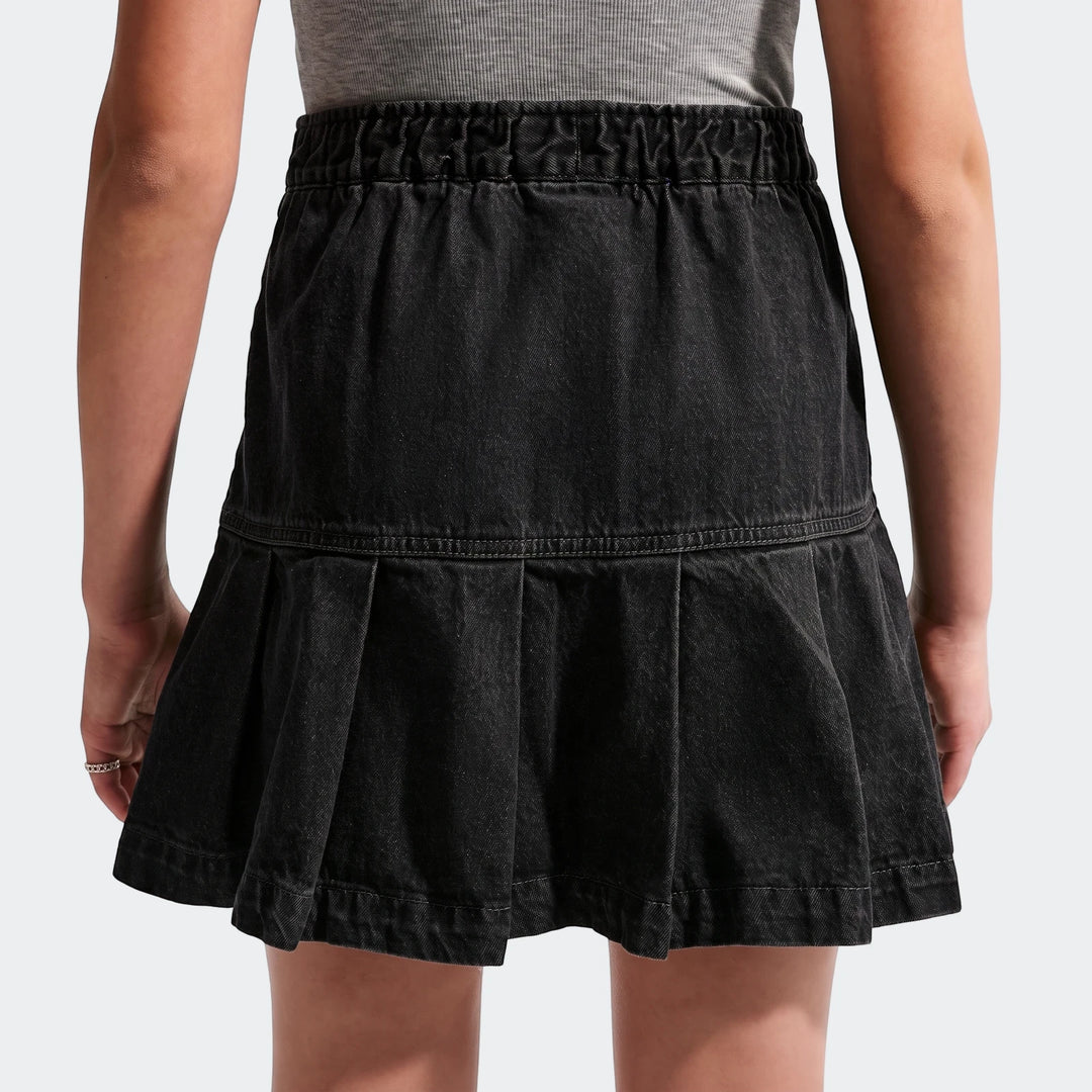 Back view of a Nike Sportswear Big Kids' (Girls') black denim pleated skirt, worn by a child.