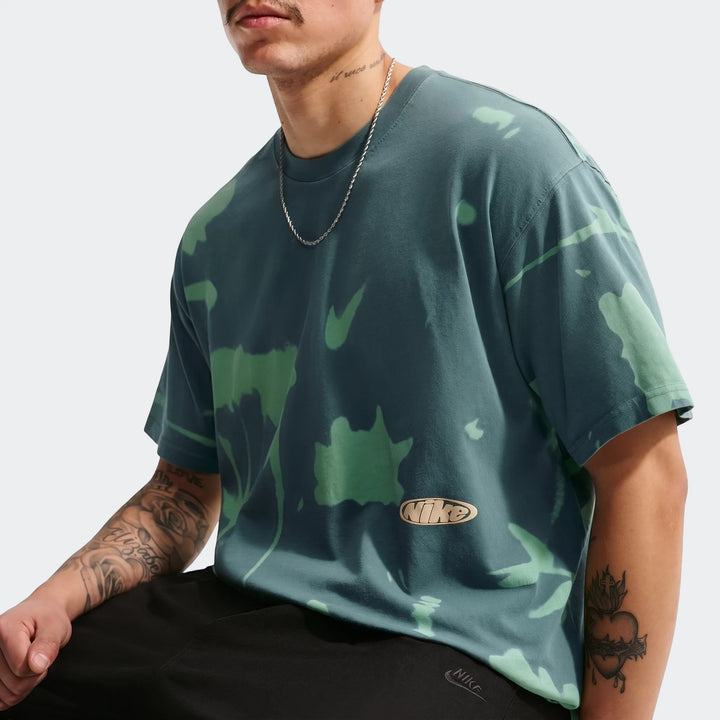 Male model wearing a Nike Sportswear Green T-shirt with a unique dark teal tie-dye pattern. Close-up view.