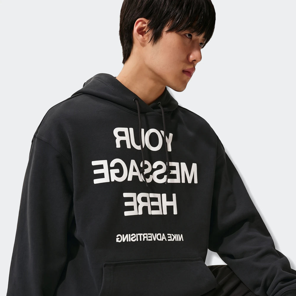 Nike Sportswear men's black fleece pullover hoodie with reversed text graphic worn by a male model.