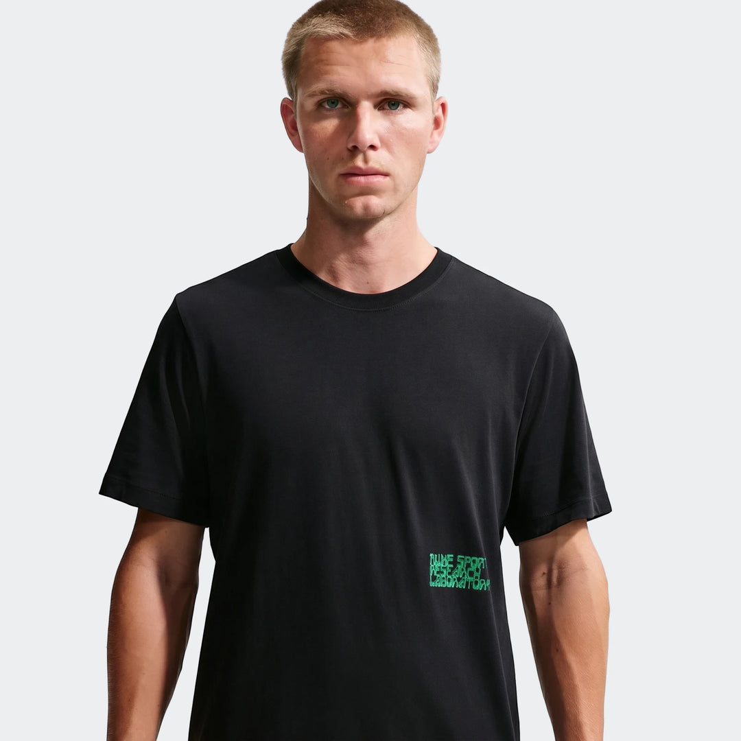 Male model wearing a black Nike Sportswear t-shirt with green graphic print, front view.