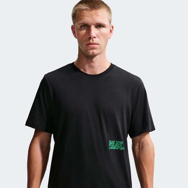 Male model wearing a black Nike Sportswear t-shirt with green graphic print, front view.