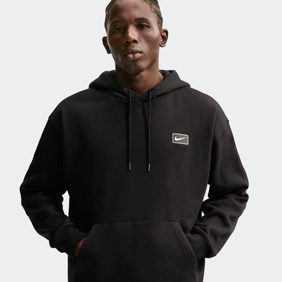 Nike Sportswear men's black pullover hoodie worn by a model, featuring a white embroidered Nike swoosh logo on the chest.