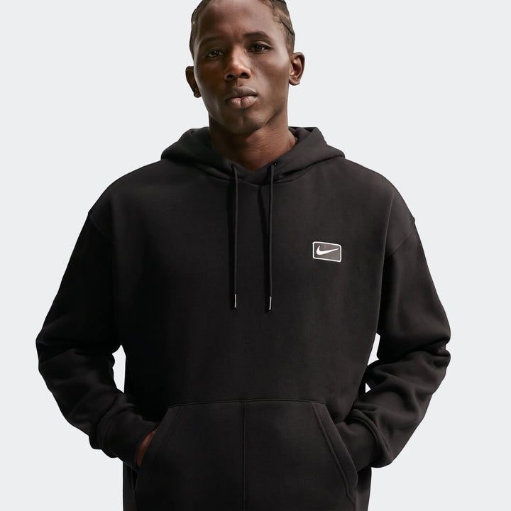 Nike Sportswear men's black pullover hoodie worn by a model, featuring a white embroidered Nike swoosh logo on the chest.