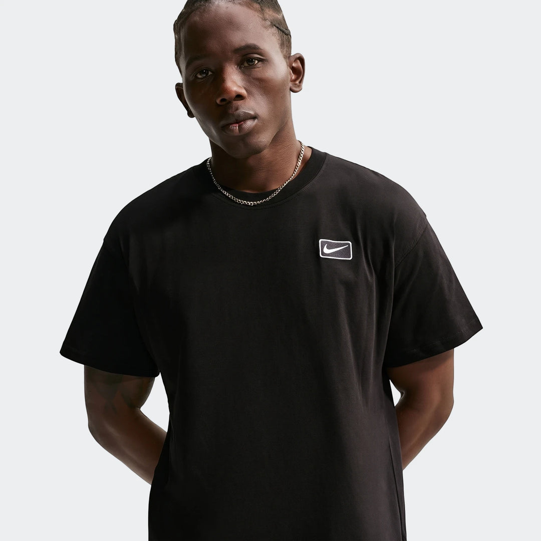 A Black male model wearing a black Nike Sportswear short-sleeve t-shirt with a white Nike logo patch and a silver chain