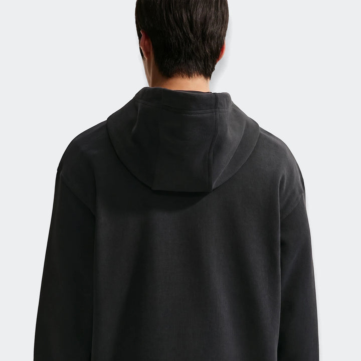A man wears a black Nike Sportswear Men's Fleece Pullover Hoodie, viewed from the back, showcasing the soft fleece fabric