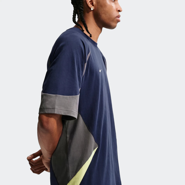 Side profile of a male model wearing a Nike Sportswear men's navy blue, grey, and neon yellow short-sleeve top.