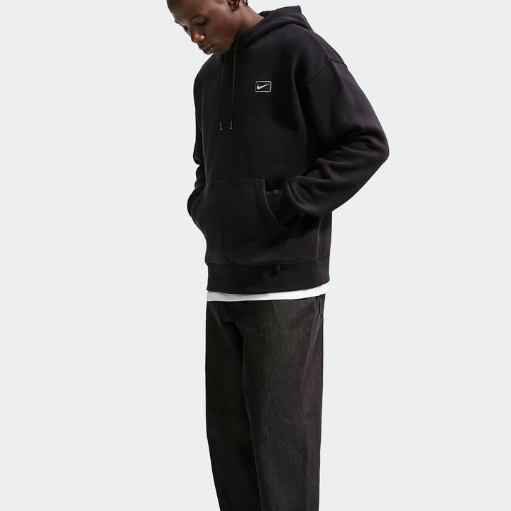Black Nike Sportswear Men's Pullover Hoodie worn by a man in a side profile view, with hands in the kangaroo pocket.