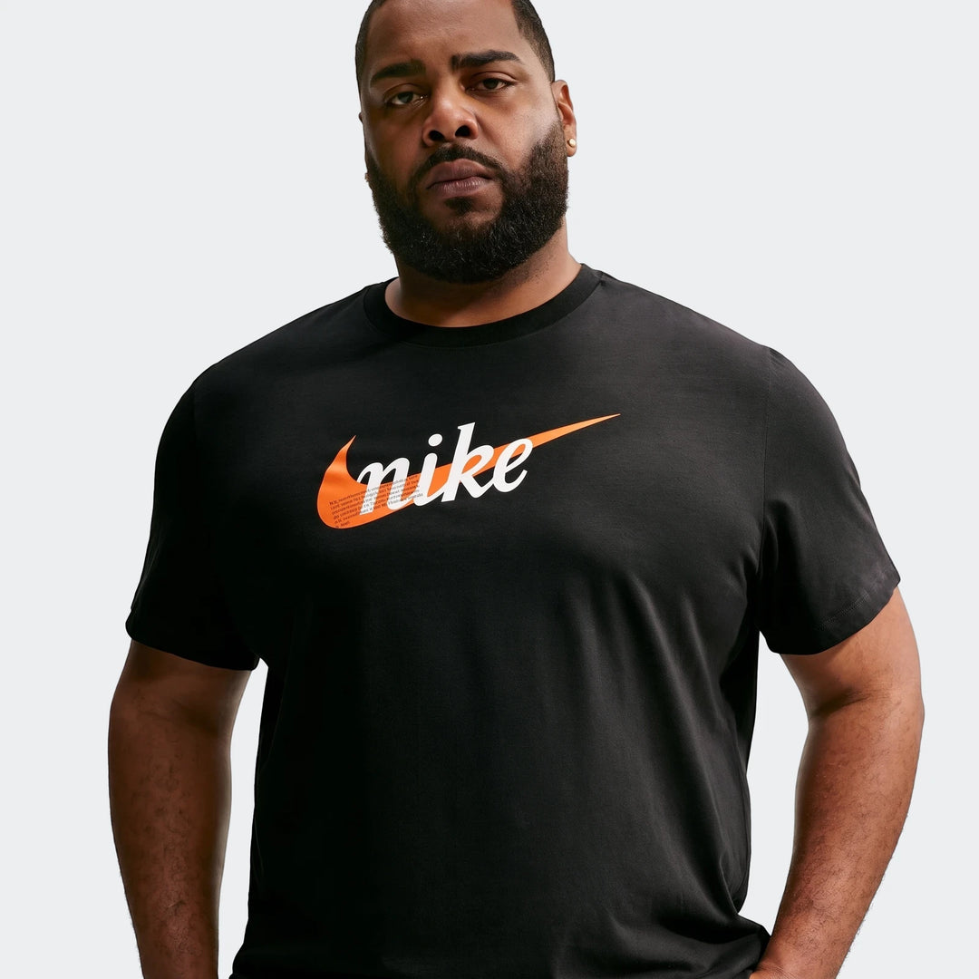 Man wearing a black Nike Sportswear Men's T-Shirt with an orange and white logo, short sleeves, posing against a light