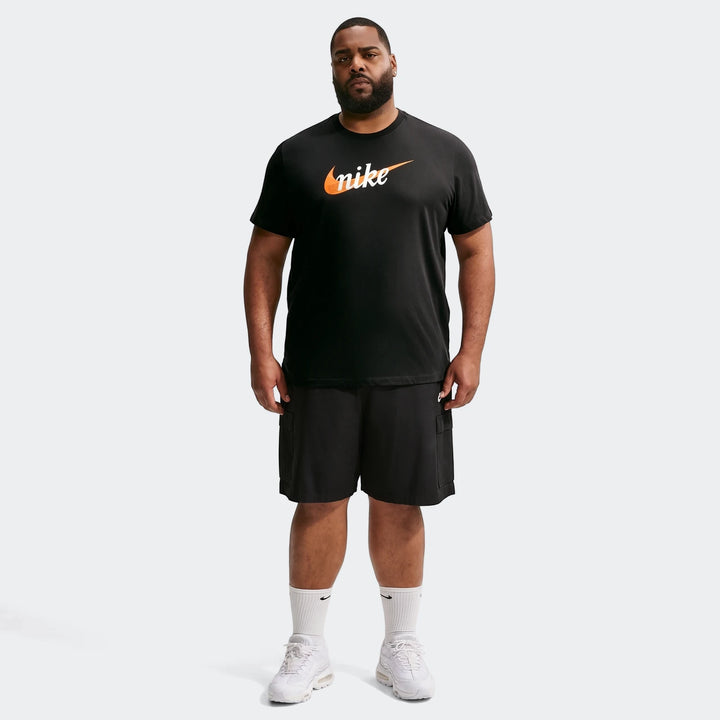 Full-body shot of a man wearing a black Nike Sportswear men's t-shirt, black cargo shorts, white socks, and white sneakers.