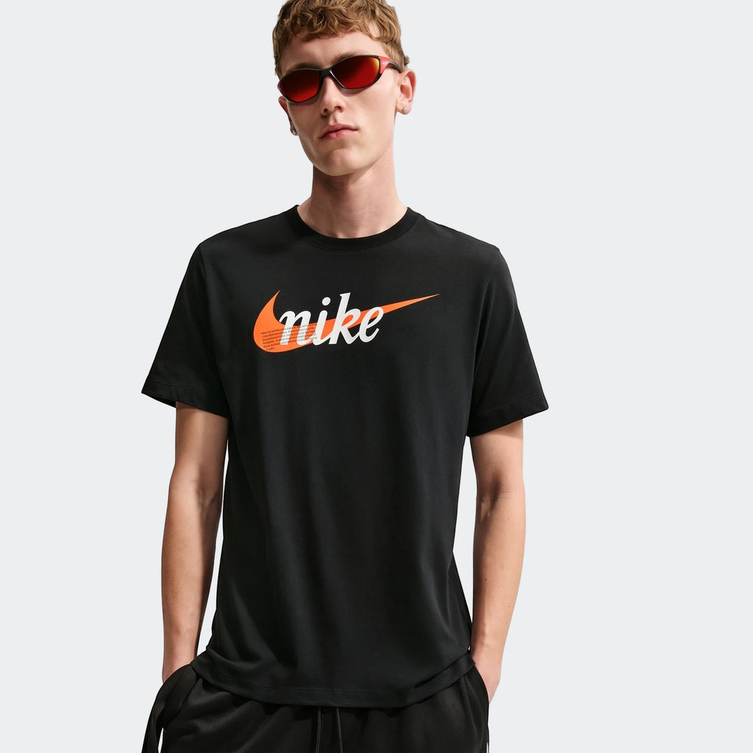 A male model wears a black Nike Sportswear short-sleeve t-shirt with an orange and white graphic logo. He is also wearing
