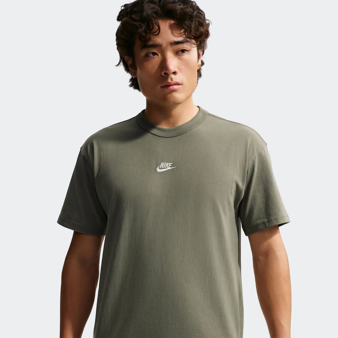 Front view of a man wearing a Nike Sportswear Premium Essentials green short-sleeved t-shirt with a white logo on the chest.