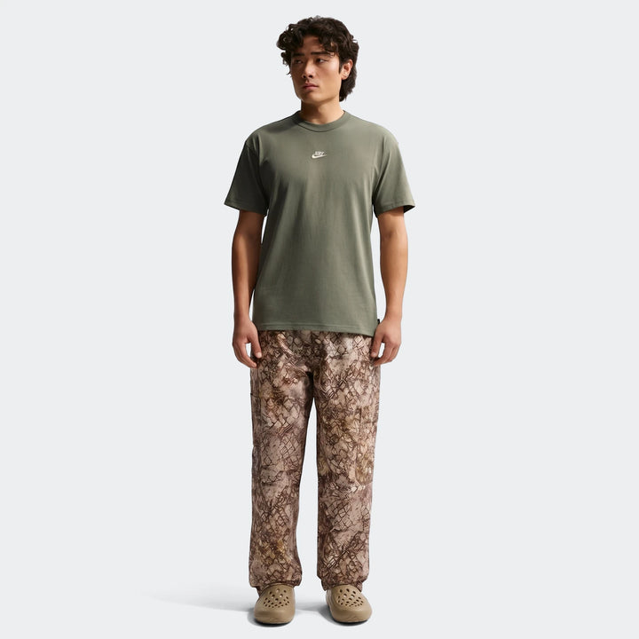 Full-body shot of a man wearing a Nike Sportswear Premium Essentials green t-shirt, brown patterned cargo pants, and tan