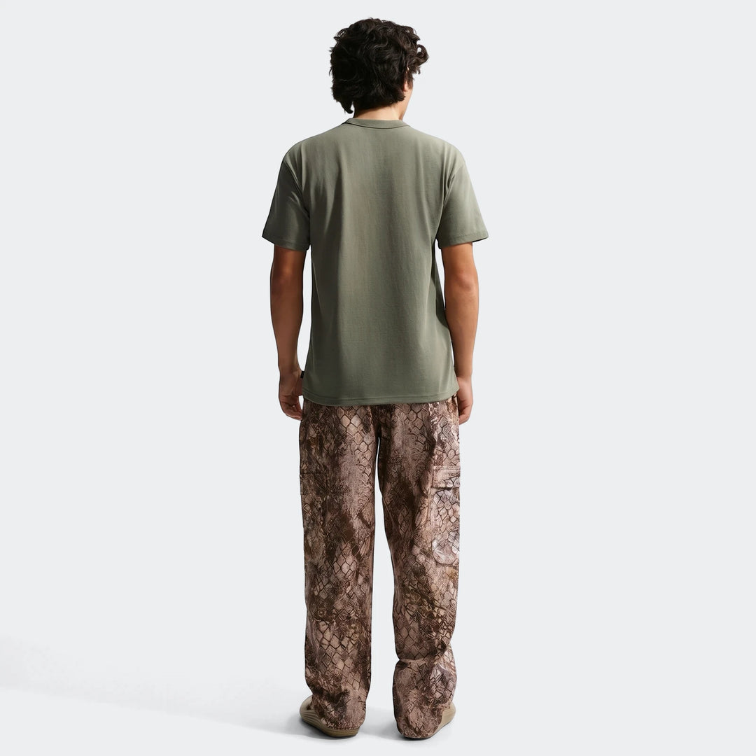 Back view of a man wearing a Nike Sportswear Premium Essentials olive green t-shirt and brown snake-print cargo pants.