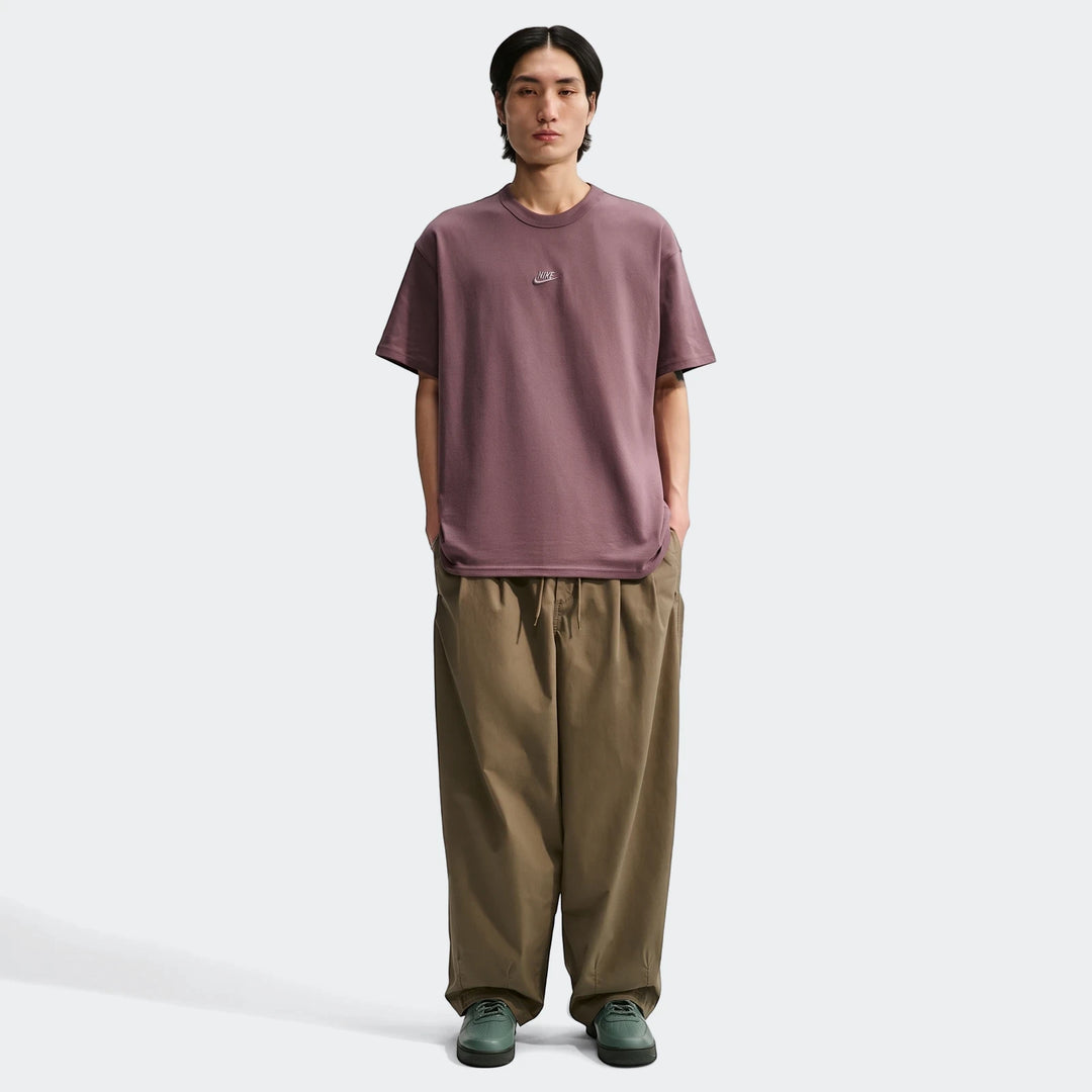 Full-body shot of a male model wearing a plum Nike Sportswear Premium Essentials men's t-shirt, khaki wide-leg pants, and
