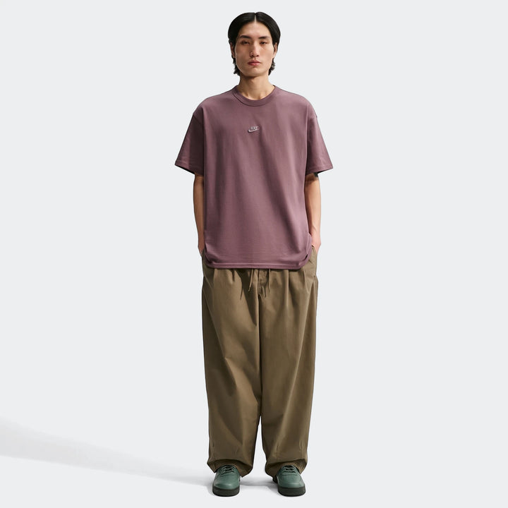 Full-body shot of a male model wearing a plum Nike Sportswear Premium Essentials men's t-shirt, khaki wide-leg pants, and