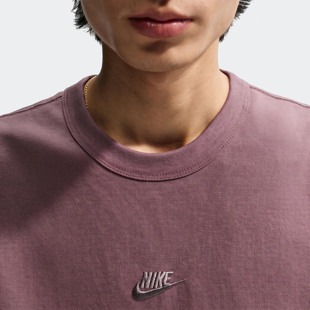 Close-up of a man wearing a mauvy-brown Nike Sportswear Premium Essentials Men's T-shirt with an embroidered logo and a gold