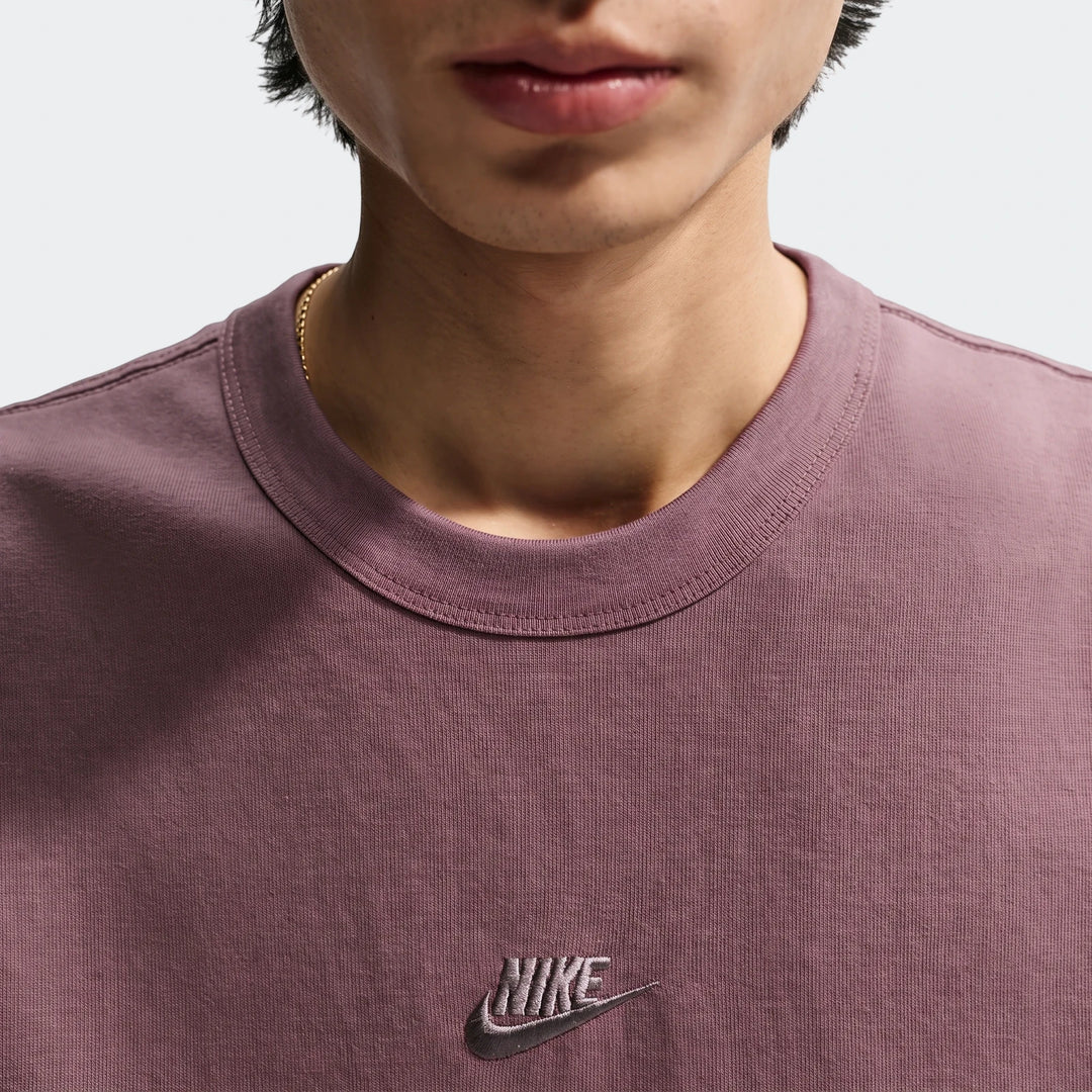 Close-up of a man wearing a mauvy-brown Nike Sportswear Premium Essentials Men's T-shirt with an embroidered logo and a gold