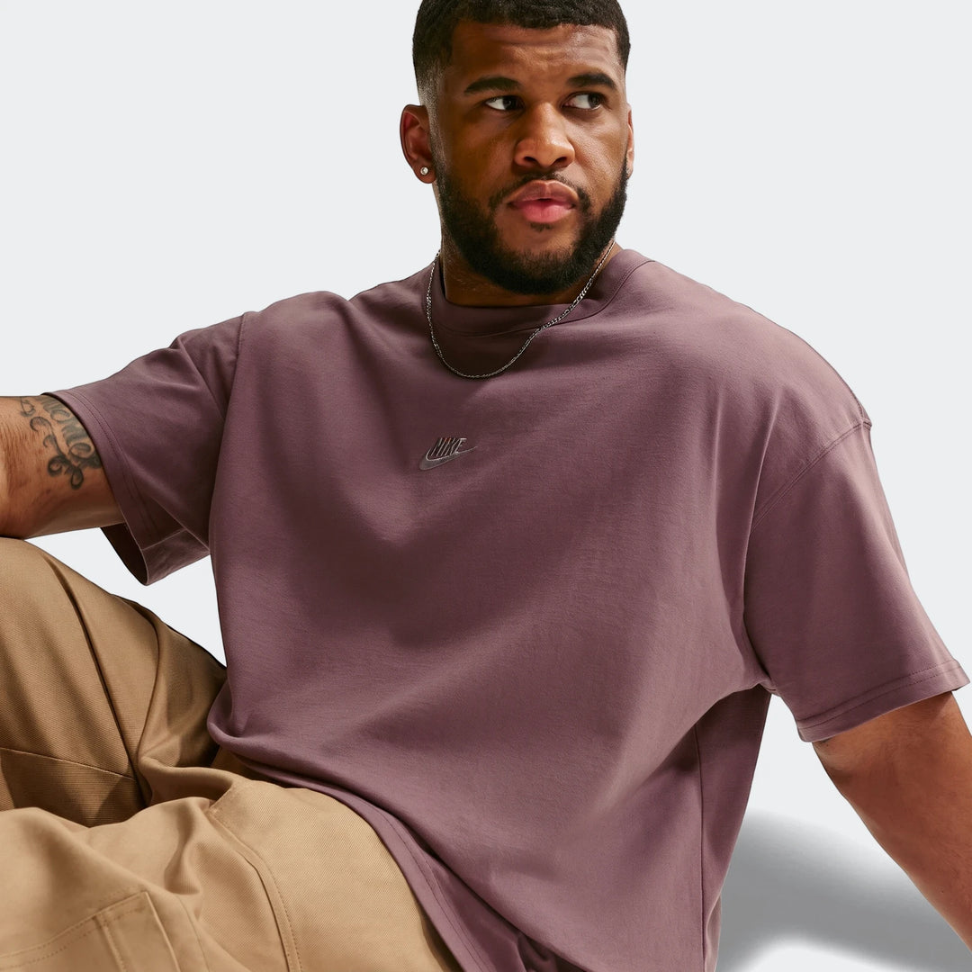 Man wearing a dusty purple Nike Sportswear Premium Essentials Men's T-Shirt with an oversized fit, sitting and looking right.