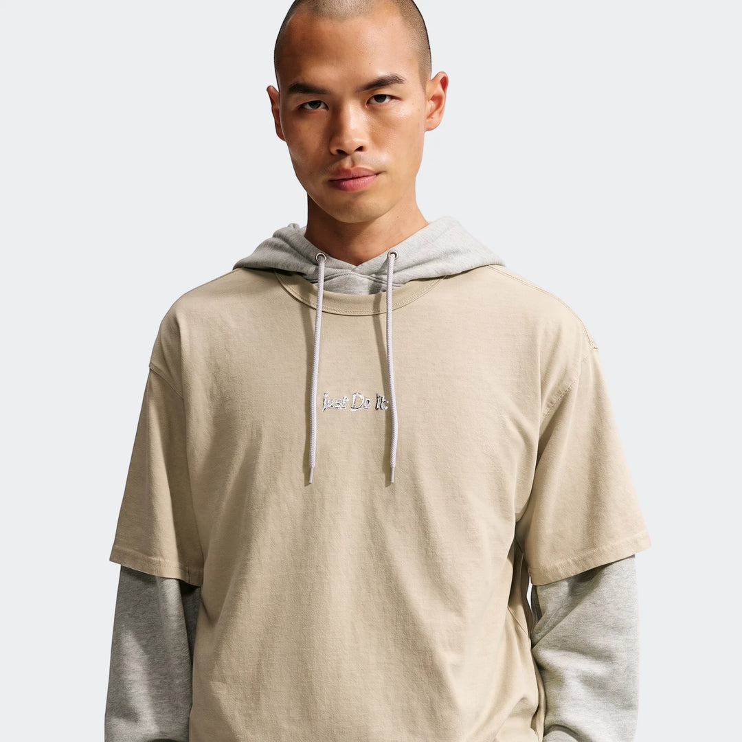 Male model showcasing a Nike Sportswear Premium Essentials T-Shirt in beige, layered over a grey hoodie, on a clean studio