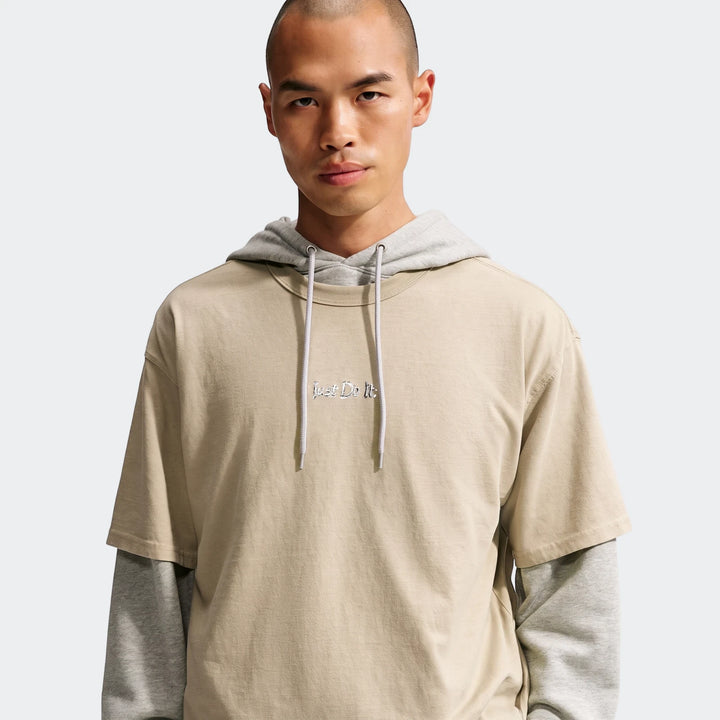 Male model showcasing a Nike Sportswear Premium Essentials T-Shirt in beige, layered over a grey hoodie, on a clean studio