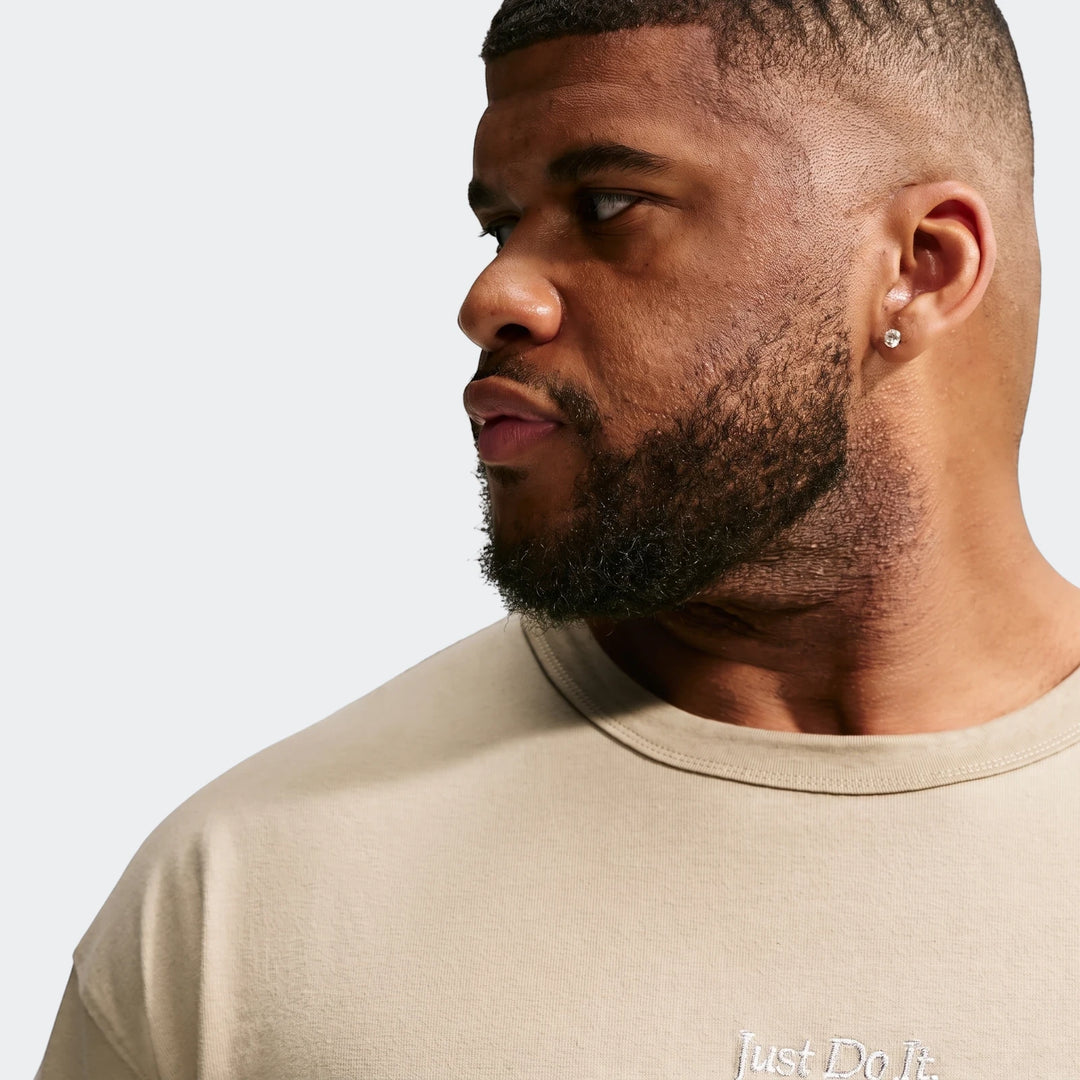 Close-up of a man wearing a beige Nike Sportswear Premium Essentials T-Shirt, showing the embroidered logo.