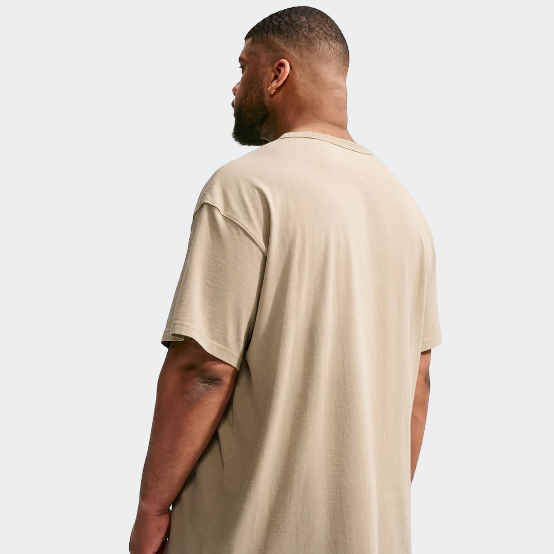 Back view of a man wearing a beige oversized Nike Sportswear Premium Essentials T-Shirt. The short-sleeve tee features