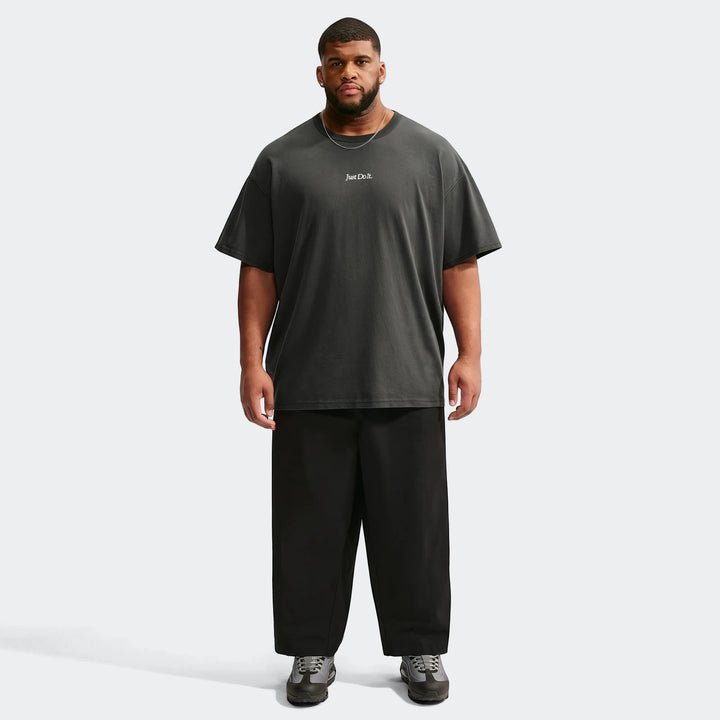 Oversized dark grey Nike Sportswear Premium Essentials T-Shirt worn by a male model, styled with black pants and sneakers,