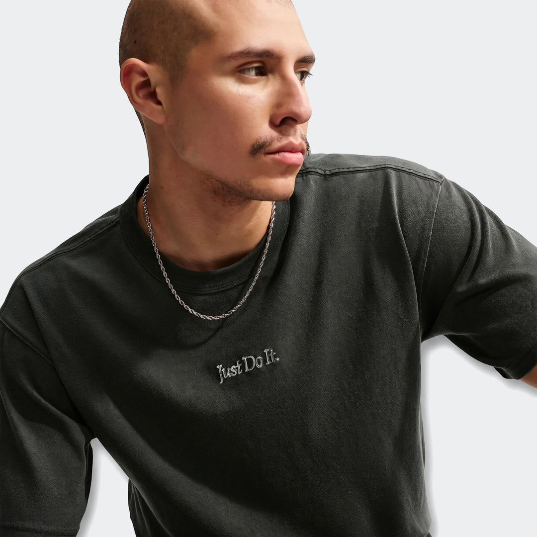 Close-up of a man wearing a dark grey Nike Sportswear Premium Essentials T-Shirt with a silver chain.