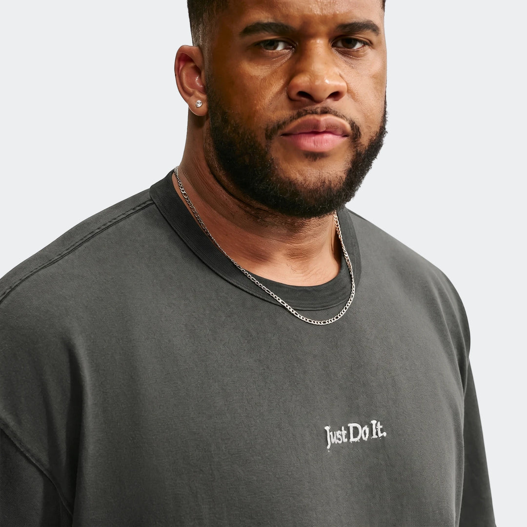 Close-up of a man wearing a dark grey Nike Sportswear Premium Essentials T-Shirt with 'Just Do It.' logo and a silver chain.