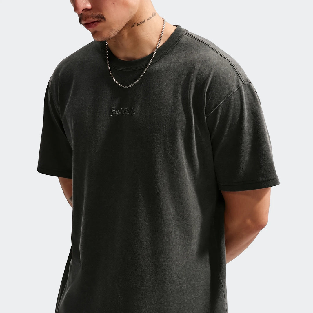Man wearing a dark grey Nike Sportswear Premium Essentials T-Shirt with 'Just Do It' logo and a silver chain.
