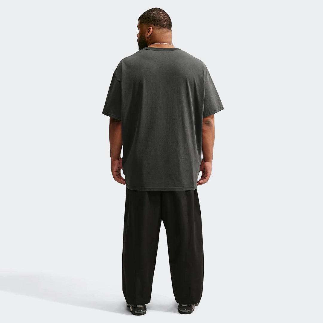 Rear view of a man wearing an oversized dark grey Nike Sportswear Premium Essentials T-shirt and black wide-leg pants.