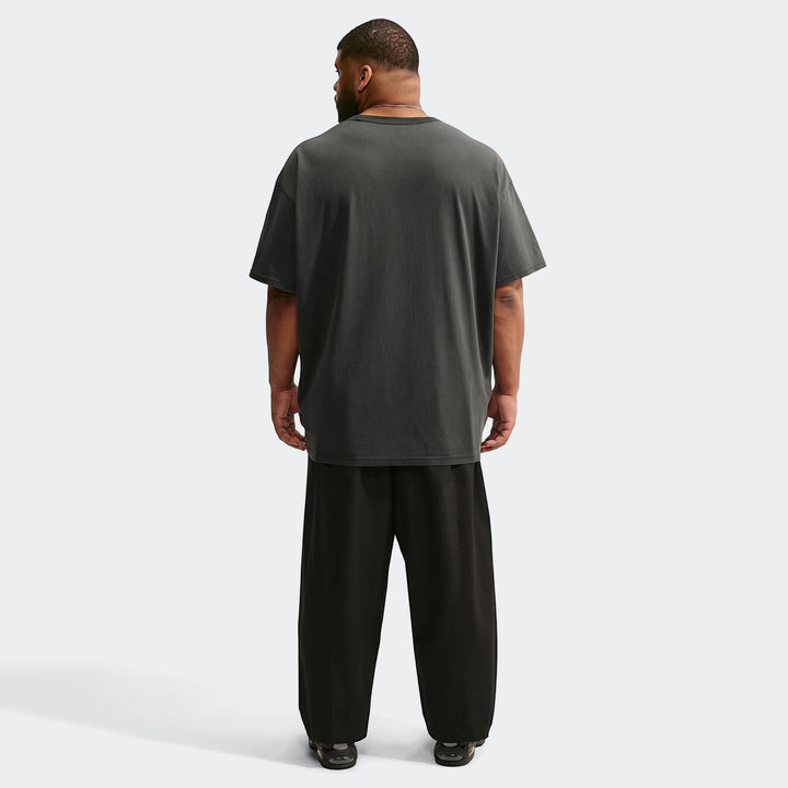 Rear view of a man wearing an oversized dark grey Nike Sportswear Premium Essentials T-shirt and black wide-leg pants.