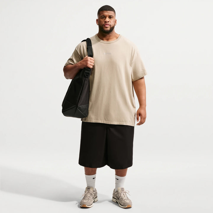 Full shot of a male model wearing a beige Nike Sportswear Premium Essentials T-Shirt, black shorts, sneakers, and carrying a