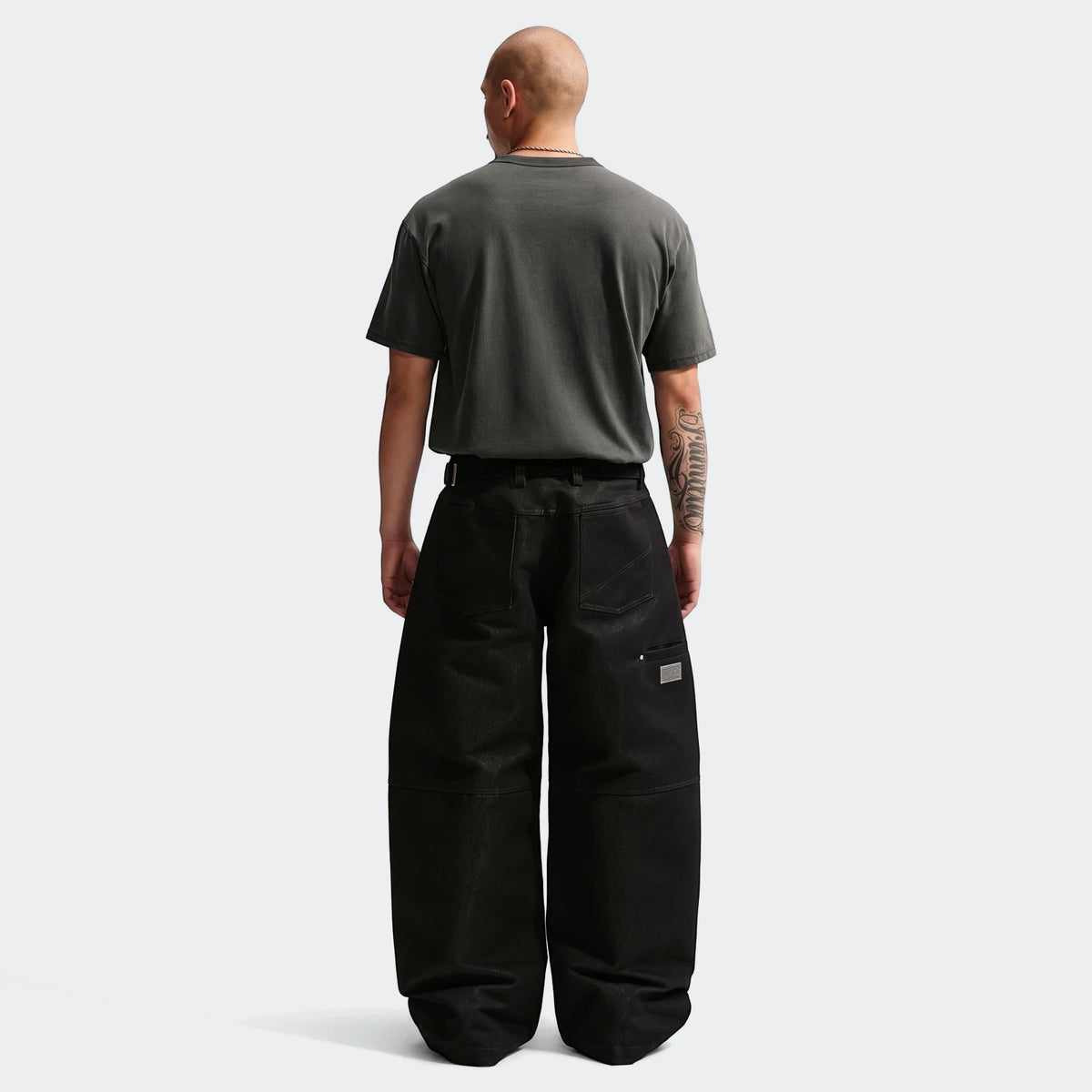 Bald man wearing a charcoal Nike Sportswear Premium Essentials T-Shirt and black wide-leg pants, shown from the back.