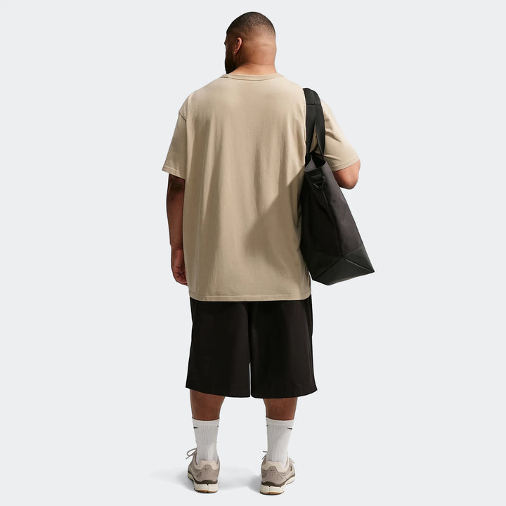 Men's Nike Sportswear Premium Essentials T-Shirt in oversized beige, paired with black shorts and a tote bag, shown from the