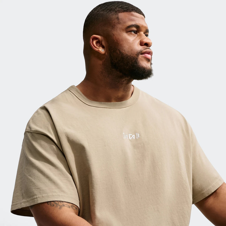 Men's beige Nike Sportswear Premium Essentials T-Shirt, featuring an embroidered 'Just Do It' logo, modeled in a close-up