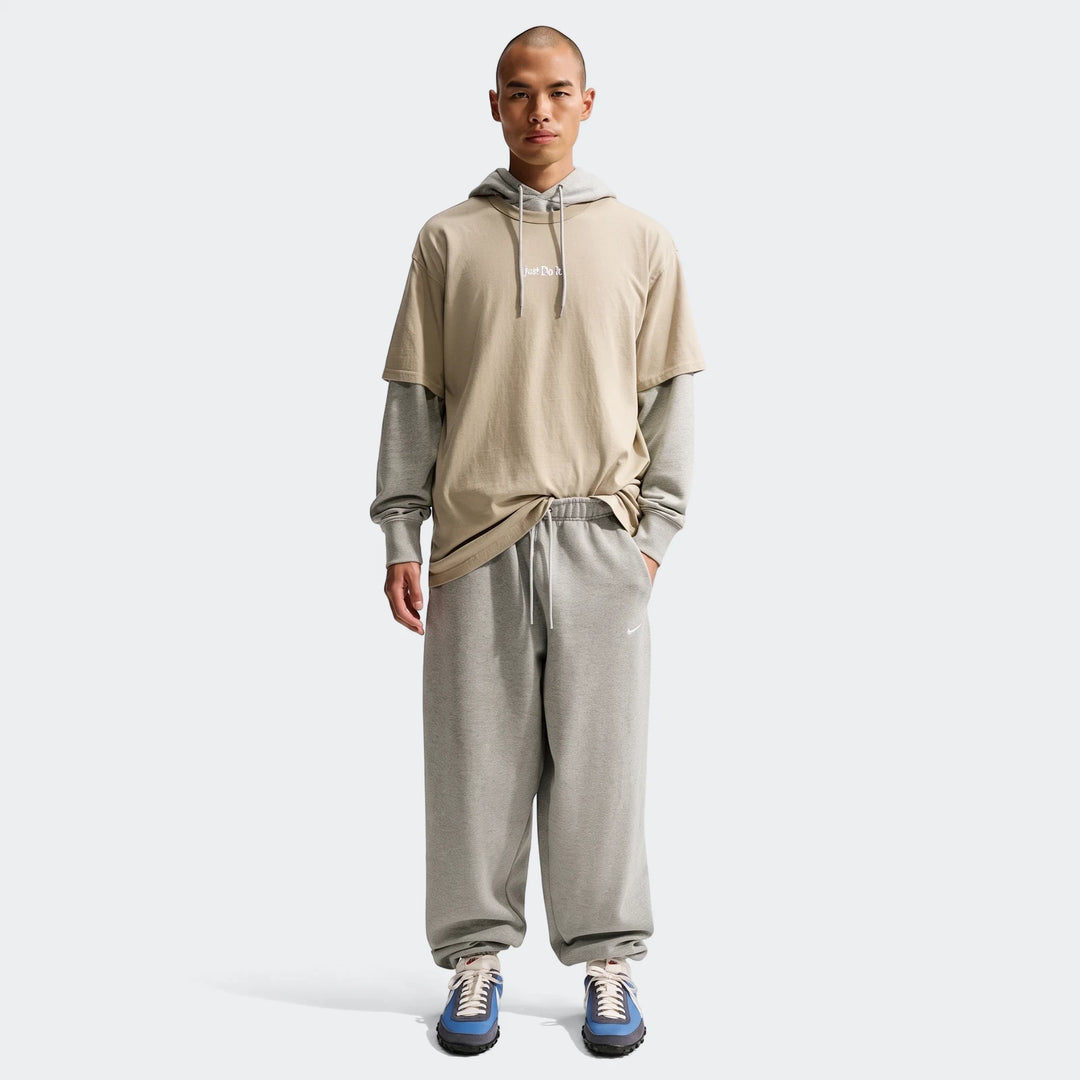 Male model wearing a Nike Sportswear Premium Essentials T-Shirt layered over a grey hoodie, grey sweatpants, and blue