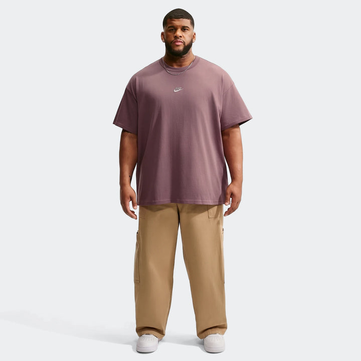 A man models a plum Nike Sportswear Premium Essentials T-shirt and khaki cargo pants, paired with white sneakers, standing