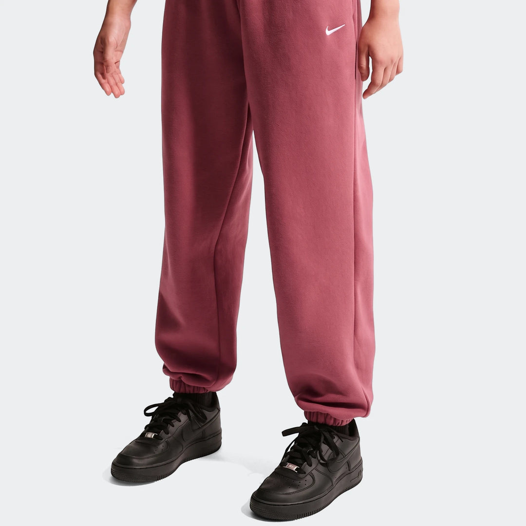 Close-up of a person wearing red Nike Sportswear Studio Fleece Girls' Loose Pants and black Nike sneakers on a white