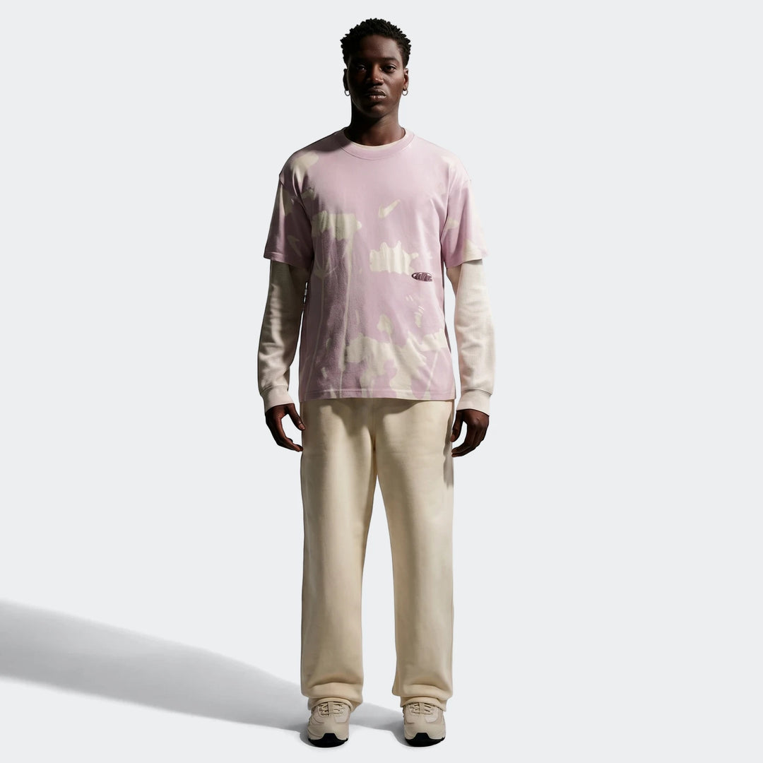 Nike Sportswear T-shirt featuring a pink and white tie-dye pattern, worn by a male model with cream sweatpants and sneakers,
