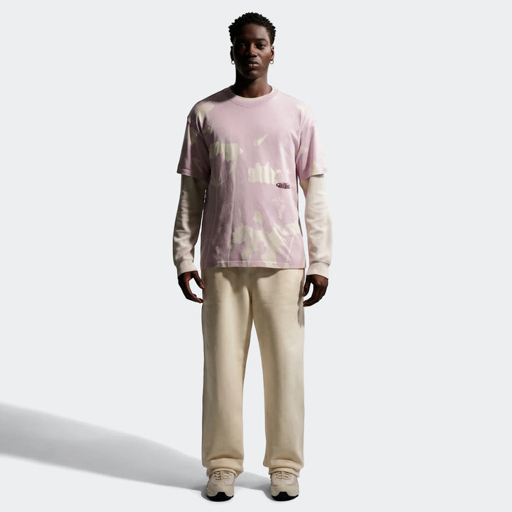 Nike Sportswear T-shirt featuring a pink and white tie-dye pattern, worn by a male model with cream sweatpants and sneakers,