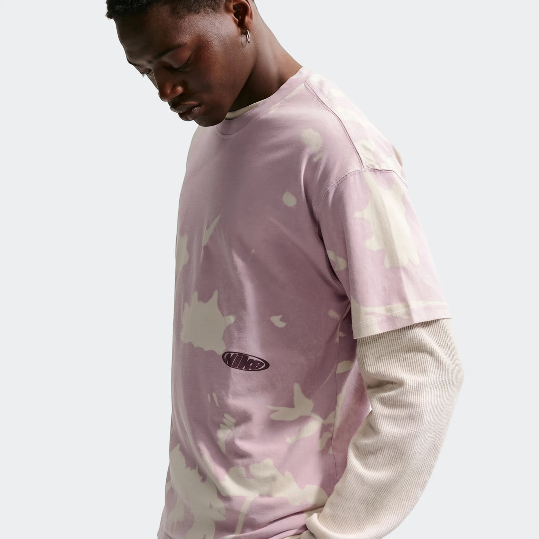 Nike Sportswear tie-dye t-shirt in purple and white, worn by a male model looking down, front view.