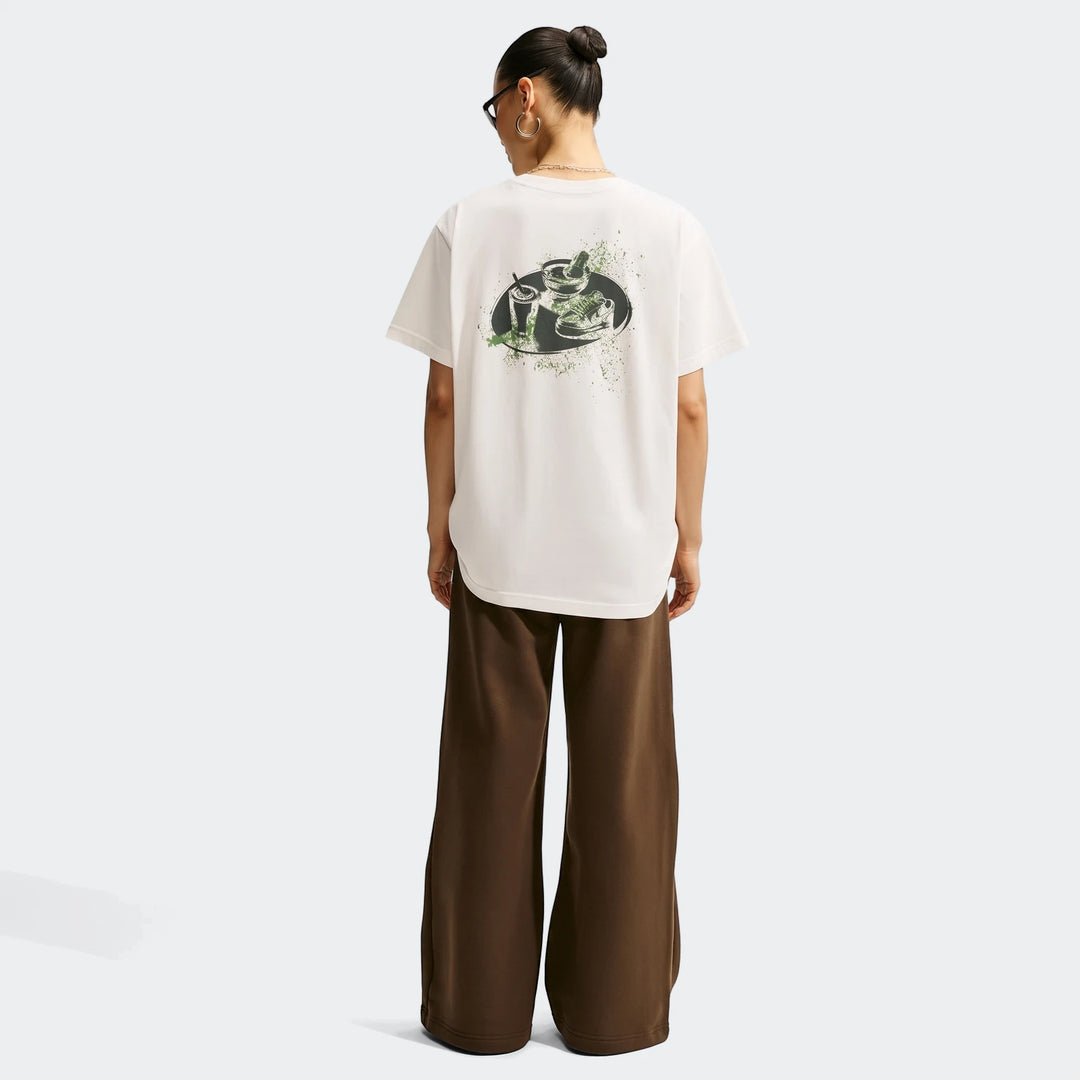 Woman in a white Nike Sportswear oversized t-shirt with a graphic print, viewed from the back, paired with brown wide-leg